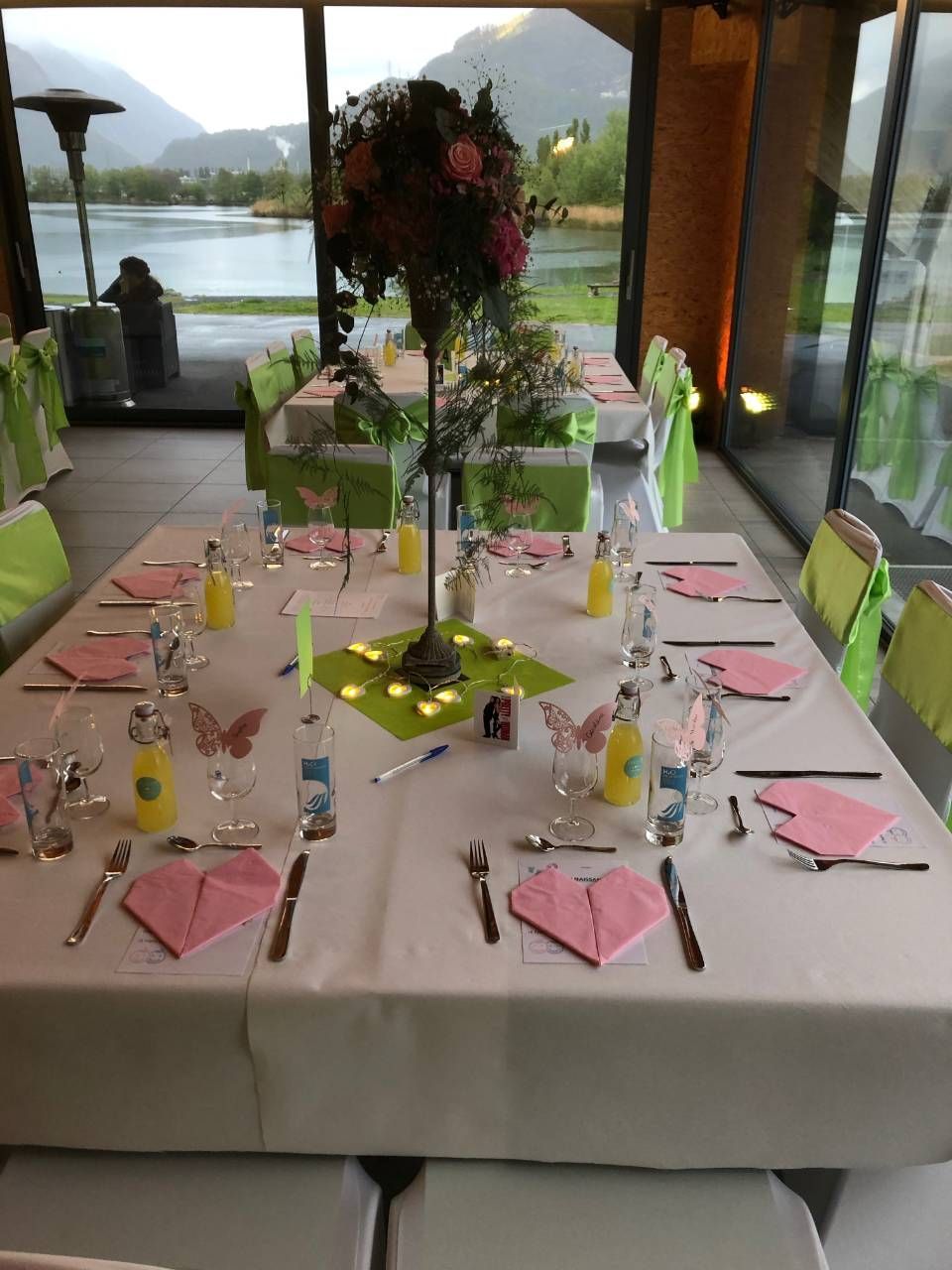 Table à manger élégante dressée avec serviettes roses et centre de table floral, avec vue sur le lac.