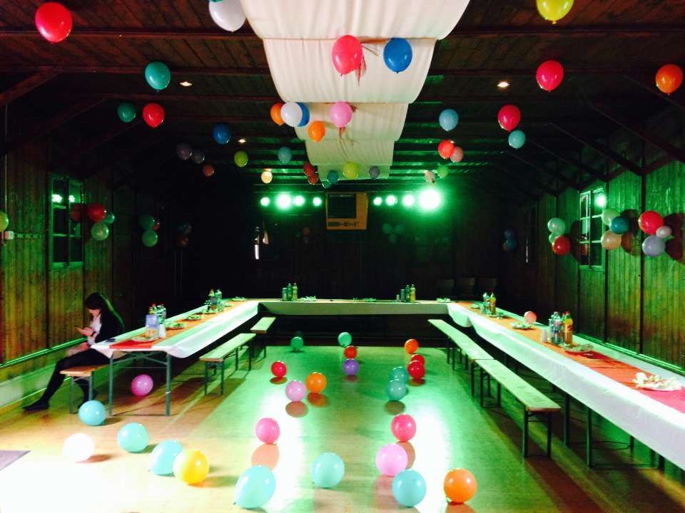 Salle de réception intérieure avec tables de banquet en forme de U, ballons colorés et éclairage de scène vert