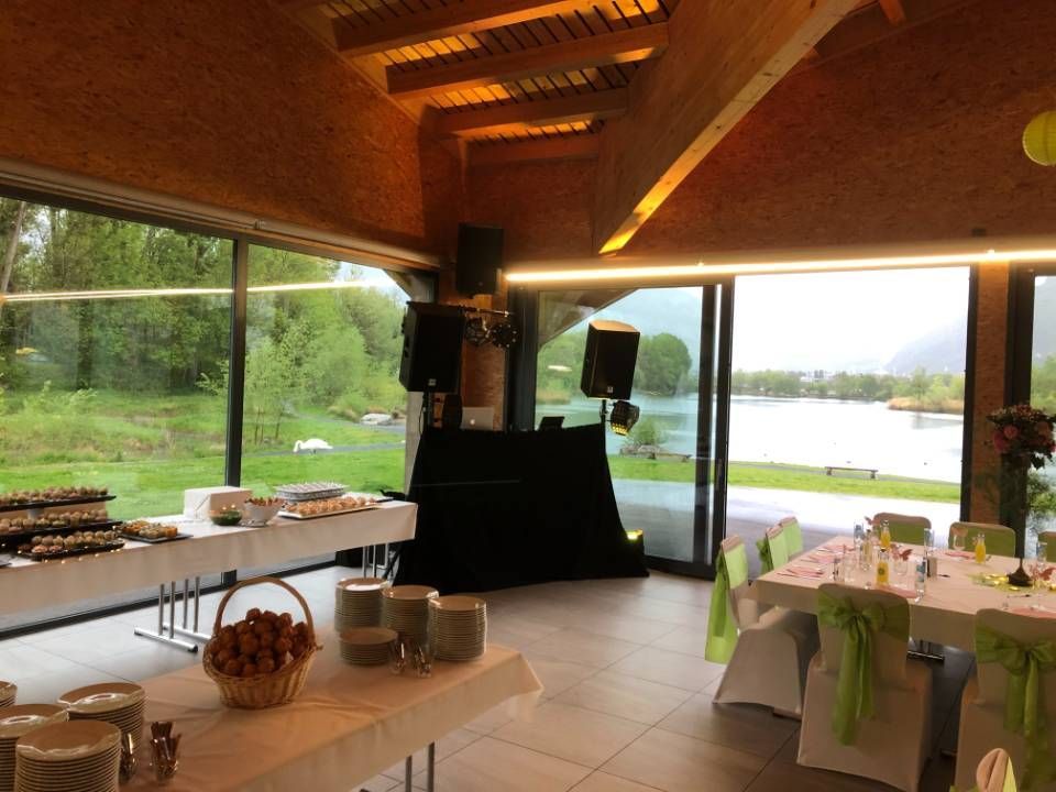 Salle à manger rustique avec tables dressées, poutres en bois et vue sur le lac à travers de grandes fenêtres.