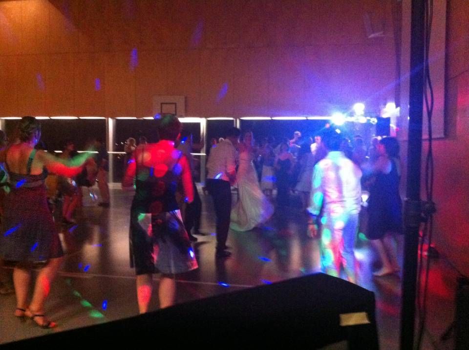 Des personnes dansent lors d'une fête faiblement éclairée par des lumières de scène colorées dans un gymnase