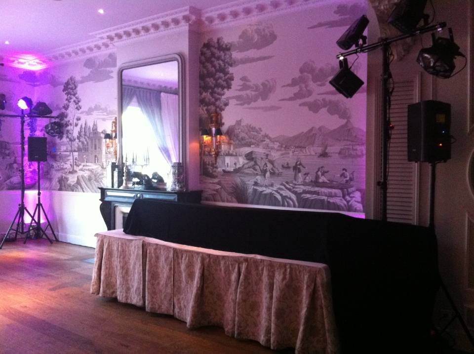Salle de réception décorée avec une longue table drapée, un éclairage violet et un mur orné d'une fresque.