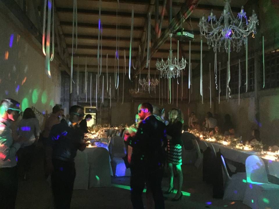 Des personnes se mêlent dans une salle faiblement éclairée, illuminée de lumières colorées et de lustres, lors d'un événement formel.