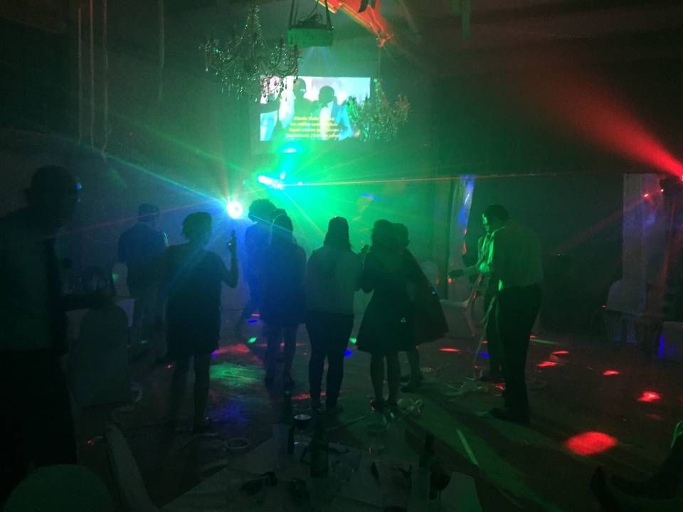 Des gens dansent dans une boîte de nuit tamisée, éclairée par des lasers verts et rouges, devant un écran de scène lumineux.