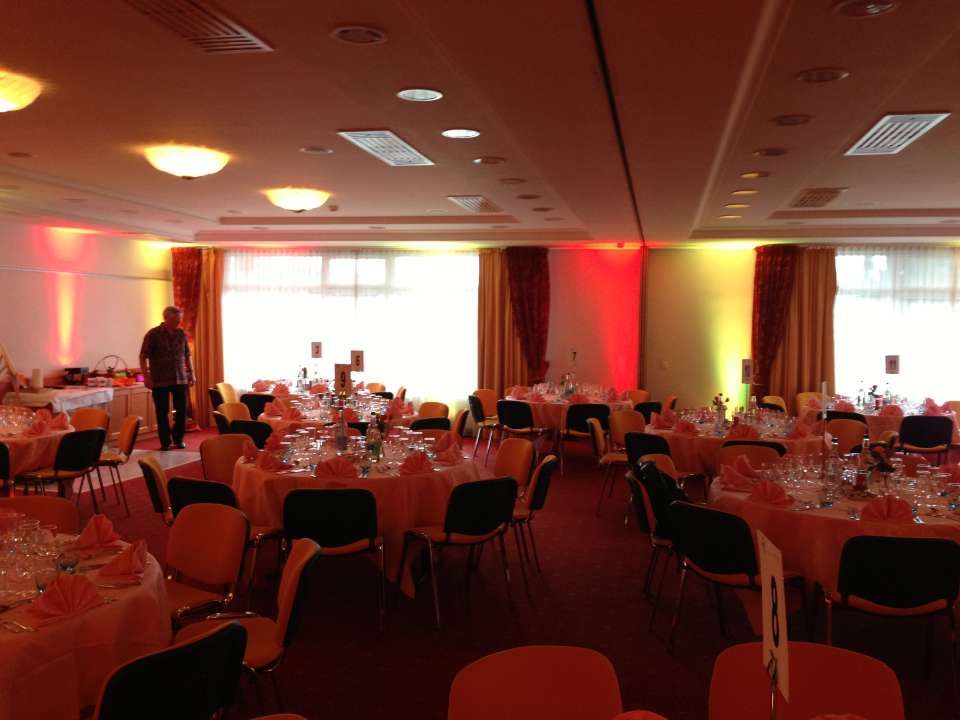 Salle de banquet avec tables rondes, éclairage d'ambiance rouge et une personne debout près du mur de gauche.