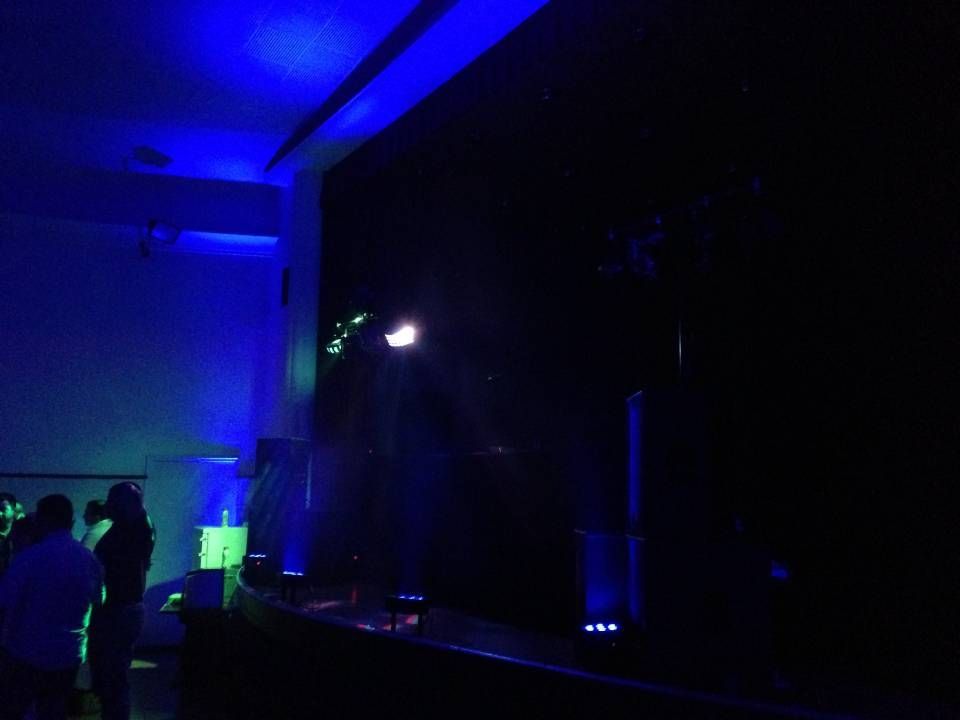 Scène sombre ou intérieur de club éclairé par des lumières bleues et vertes, avec des personnes rassemblées sur la gauche.