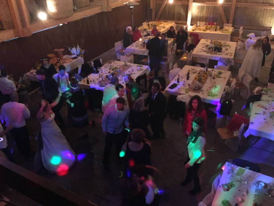 Des invités se mêlent sur une piste de danse faiblement éclairée lors d'une fête intérieure décorée de lumières colorées et de tables