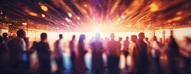 Foule floue lors d'un concert ou d'un événement illuminé par des lumières orange vif et des reflets au-dessus des têtes