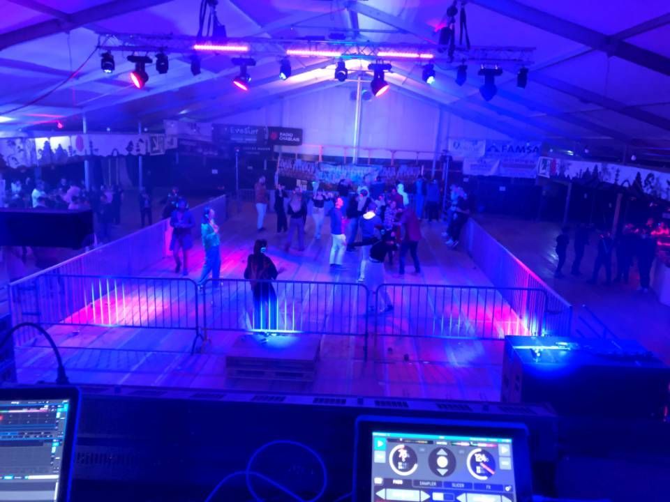Piste de danse éclairée en bleu sous une tente, avec des gens qui dansent et du matériel de DJ au premier plan.