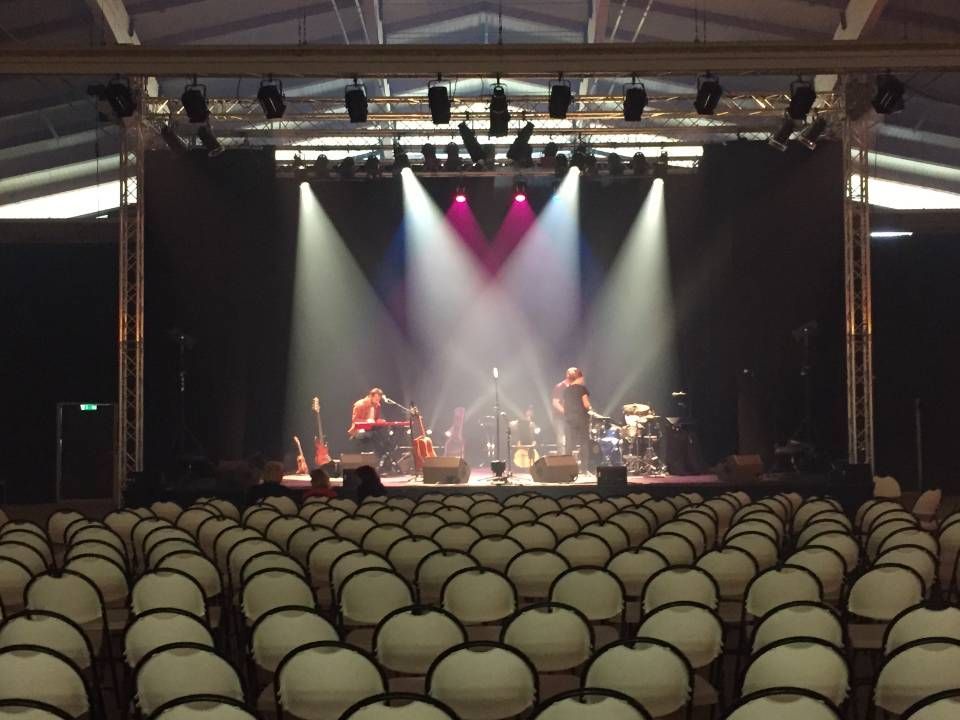 Salle de concert vide avec une scène éclairée et un groupe installé sous les projecteurs.
