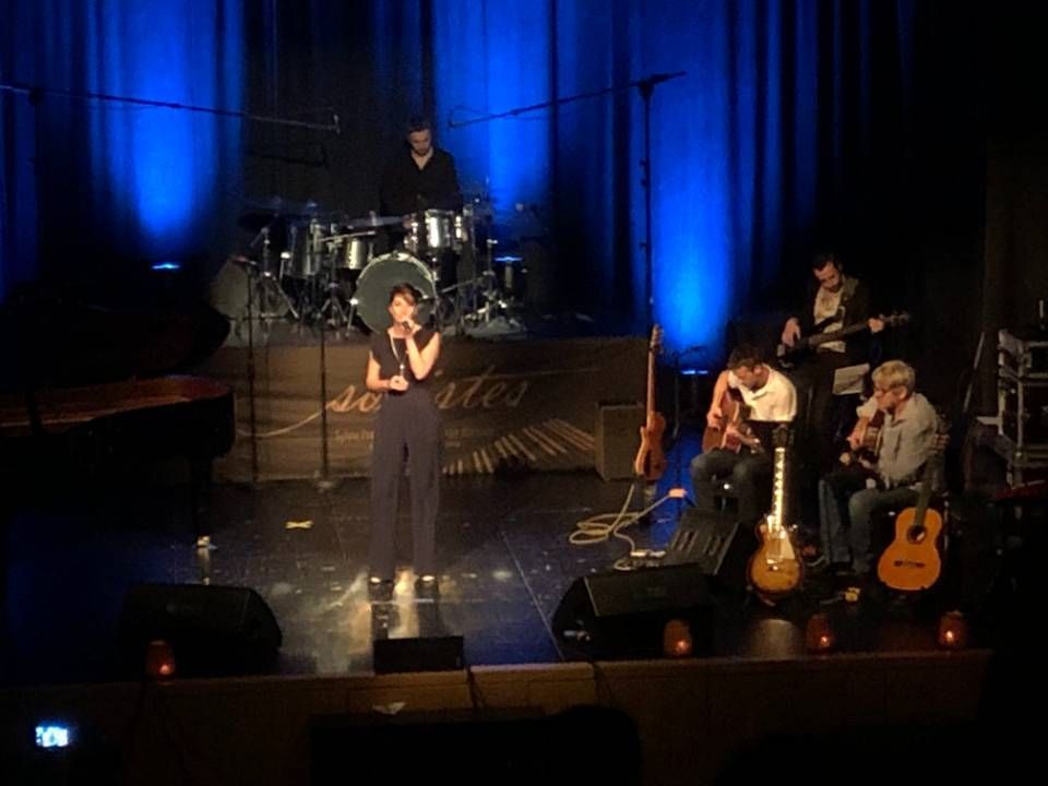Des musiciens se produisent sur une scène éclairée de bleu, le chanteur au centre et la batterie à l'arrière.