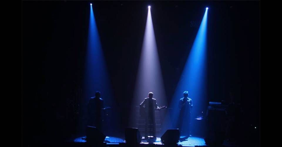 Un groupe se produit sur une scène obscure sous des projecteurs bleus et blancs.