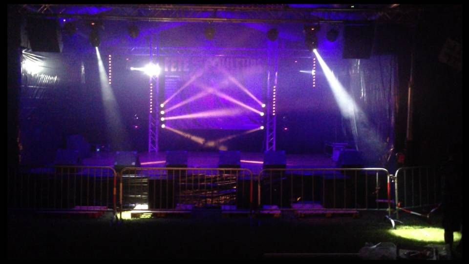 Scène vide éclairée en violet avec des projecteurs et des barrières métalliques dans une salle obscure