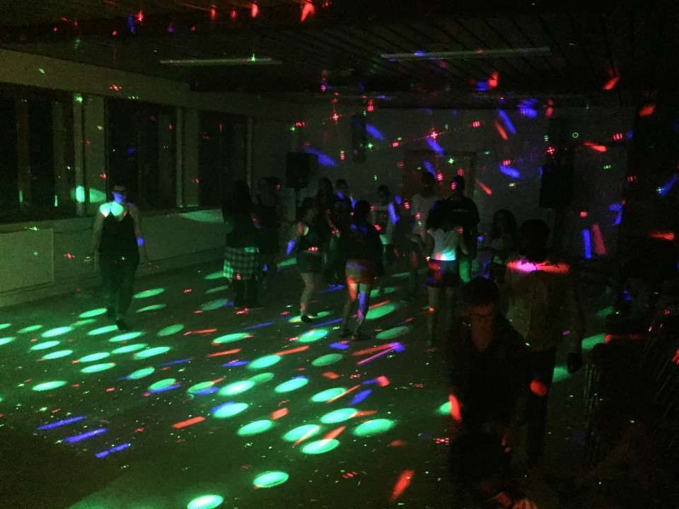 Des gens qui dansent dans une pièce sombre, des lumières laser colorées projetées sur le sol et les murs.