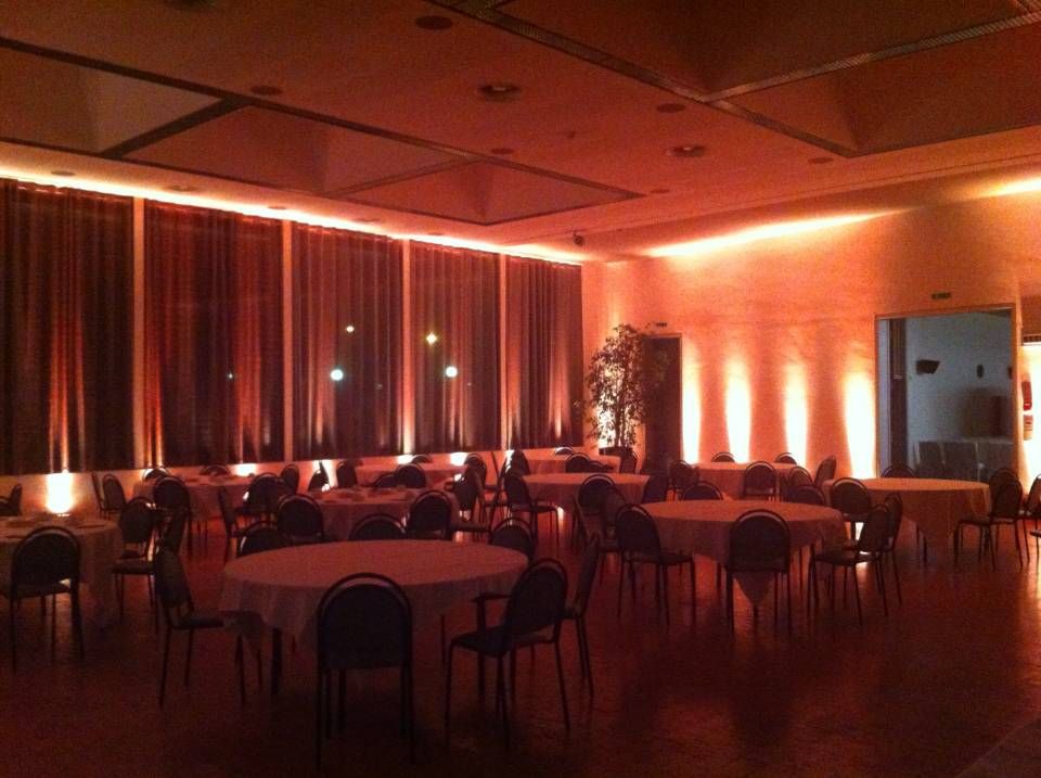 Salle de banquet à l'éclairage tamisé, avec tables rondes, chaises et éclairage orange chaud le long des murs
