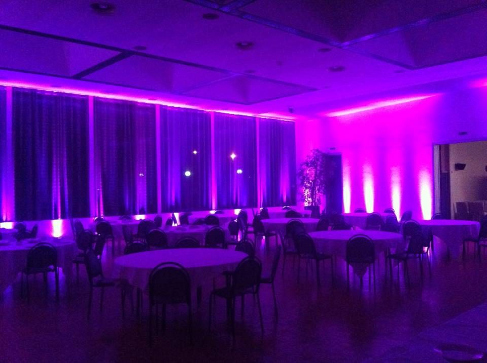 Salle de banquet éclairée de violet, avec des tables et des chaises rondes, aménagée pour un événement.