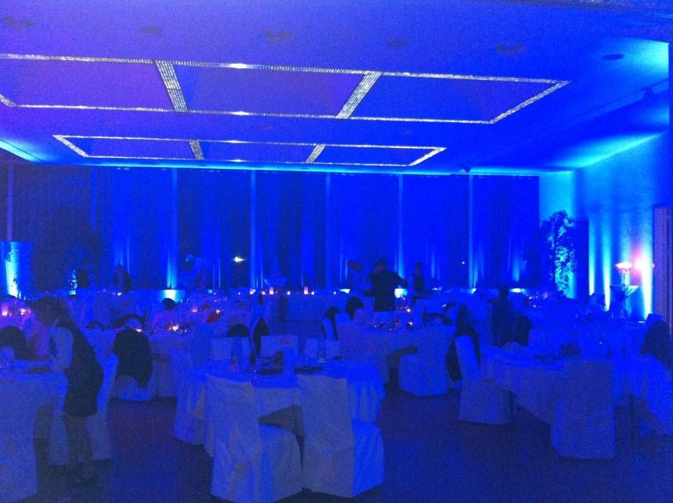 Salle de banquet éclairée en bleu avec des tables rondes dressées pour un événement et des invités assis dans la pénombre.