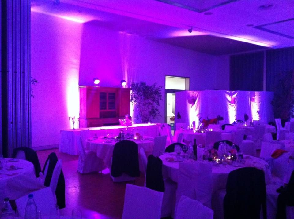 Salle de banquet éclairée en violet, avec tables et chaises décorées, prête pour un événement
