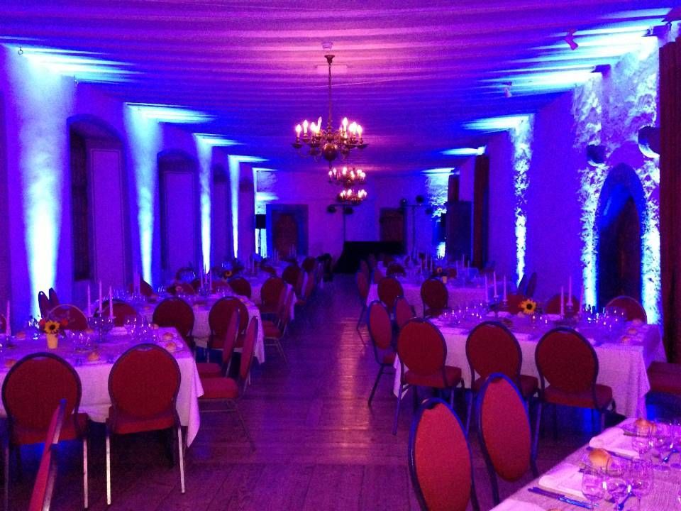 Élégante salle de banquet avec éclairage bleu-violet, tables rondes et chaises rouges, prête pour un événement.