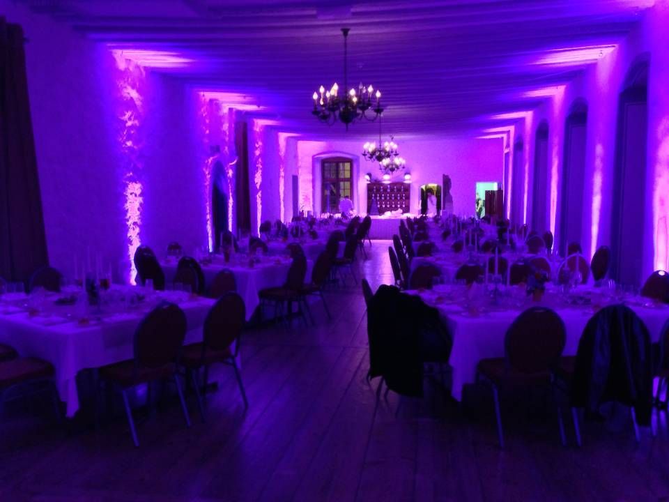 Salle de banquet éclairée de violet avec tables rondes, chaises et lustres