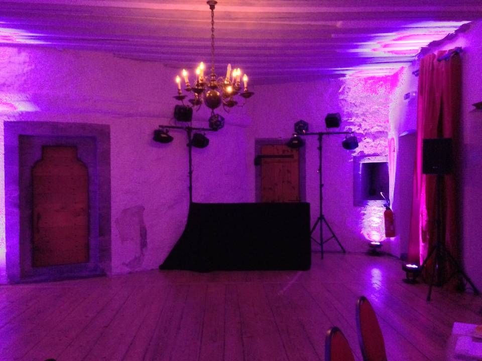 Pièce vide éclairée de violet, avec un lustre, un parquet, des rideaux rouges et une table recouverte d'une nappe contre le mur du fond.