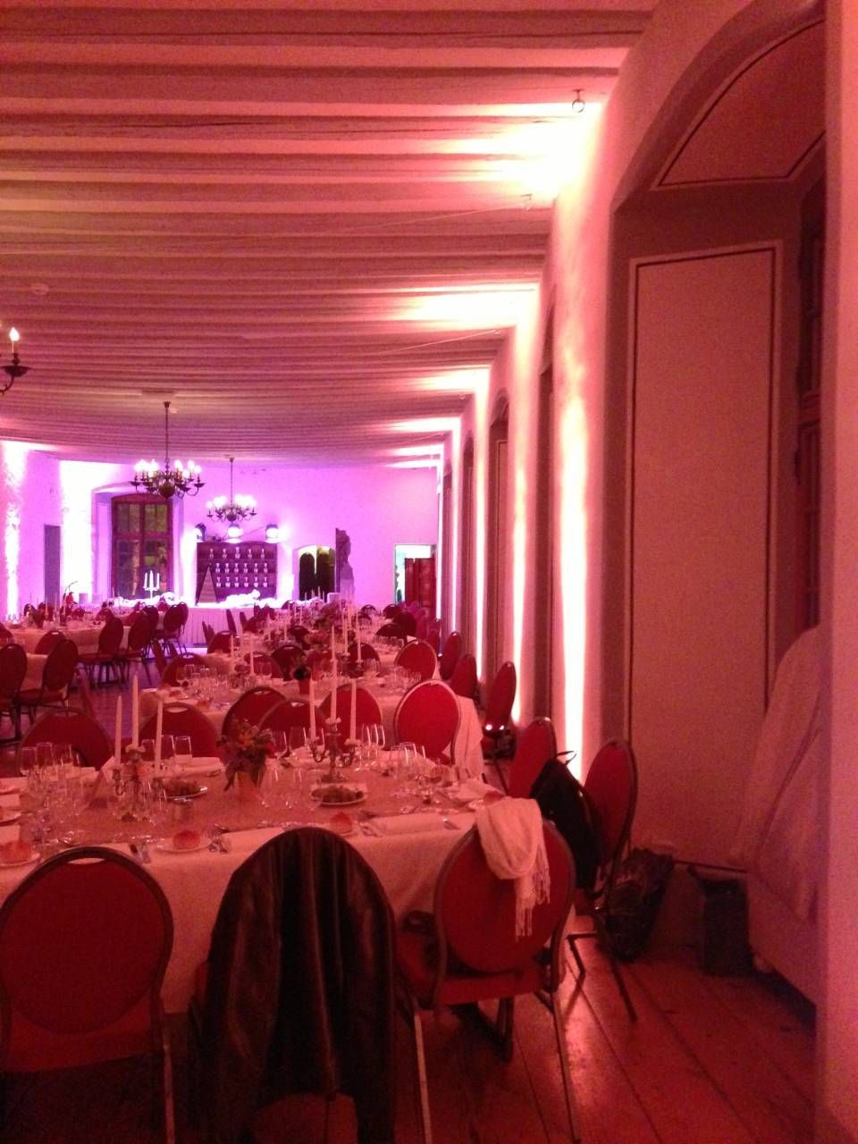 Salle de banquet élégante avec éclairage rose, tables dressées et invités assis pour un événement formel