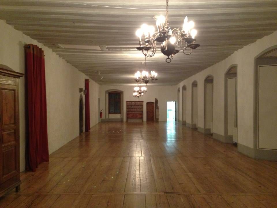 Hall élégant et vide avec parquet, lustres, rideaux rouges et portes cintrées