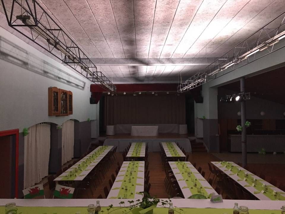 De longues tables de banquet sont dressées dans une salle faiblement éclairée, avec une estrade au fond.