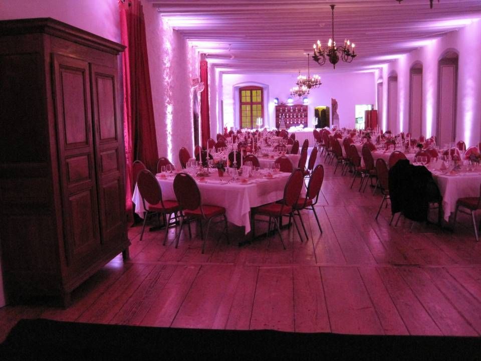 Salle de banquet éclairée à la lavande, aménagée pour un dîner formel avec des tables rondes et des lustres.