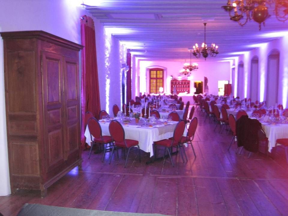Élégante salle de banquet avec nappes blanches, chaises rouges et éclairage d'ambiance violet le long d'un parquet ciré