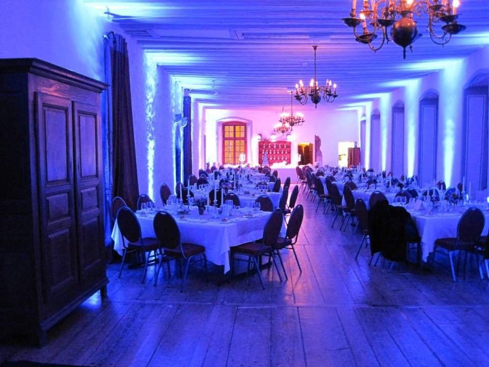 Élégante salle de banquet avec tables rondes, lustres et éclairage bleu-violet sur un parquet.