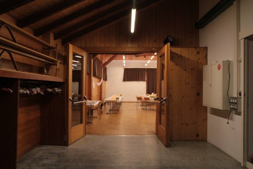 Un couloir intérieur en bois s'ouvre sur une salle de réunion lumineuse avec des tables et des chaises.
