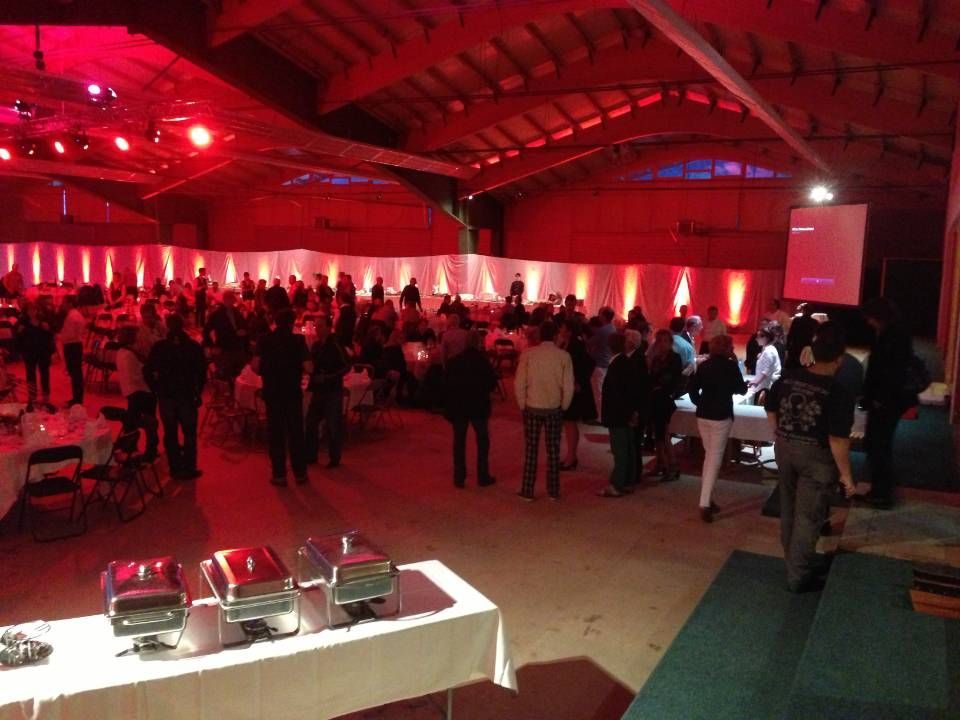 Salle de réception bondée, éclairée en rouge, où les gens se mêlent et où un écran de projection est installé à l'avant.