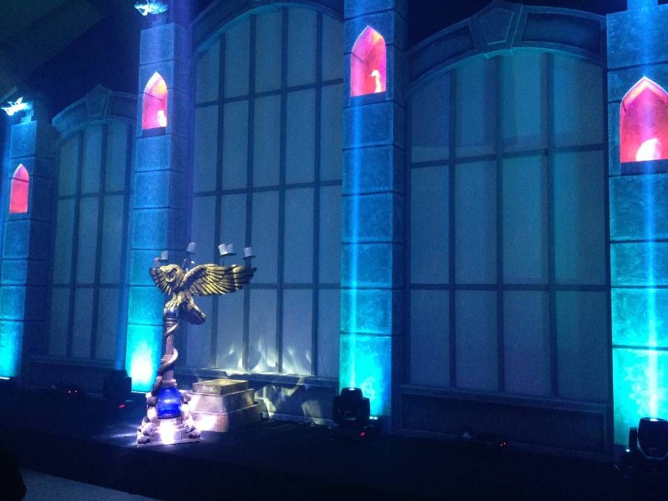 Une statue d'ange dorée illuminée en bleu et rose se détache sur un grand bâtiment la nuit.