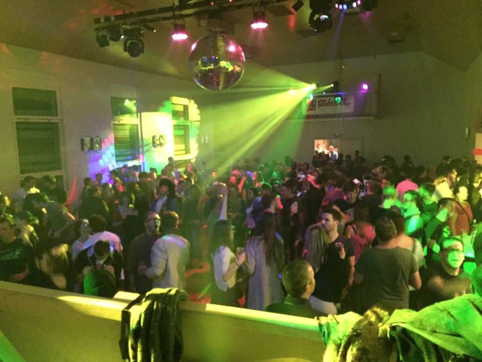 Piste de danse bondée d'une boîte de nuit, illuminée de lumières vertes et roses, avec une boule disco au plafond.