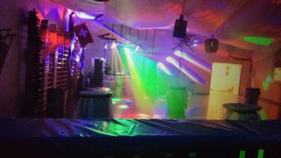Salle de fête tamisée avec lumières laser colorées, brouillard, haut-parleurs et tables sous un éclairage violet et vert