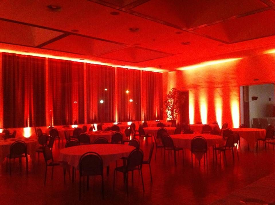 Salle de banquet éclairée en rouge avec tables rondes, chaises et rideaux drapés