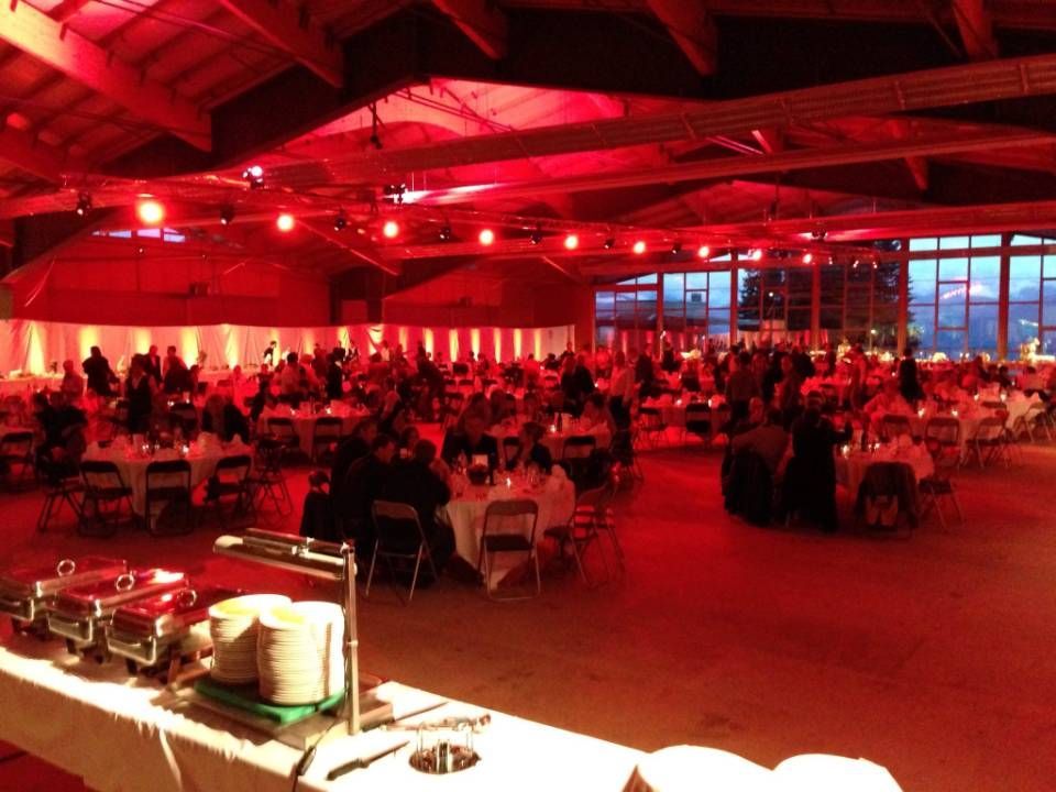 Salle de banquet éclairée de rouge, avec de nombreux invités assis à des tables rondes sous un plafond en bois
