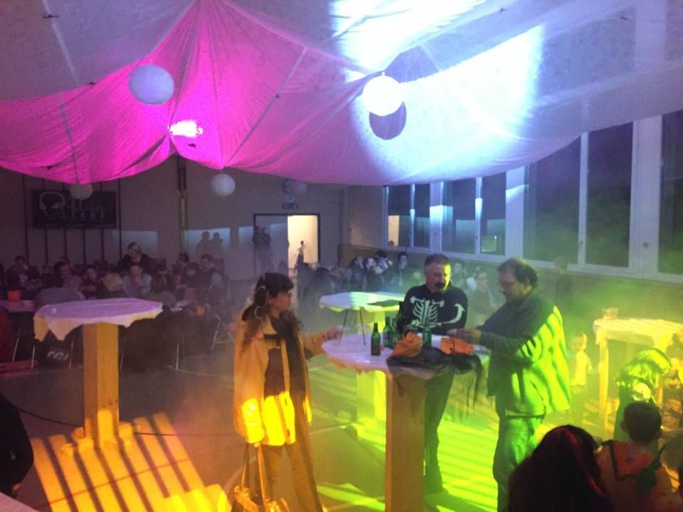 Des personnes discutent dans un espace événementiel coloré et brumeux, illuminé de rose, de bleu et de vert.