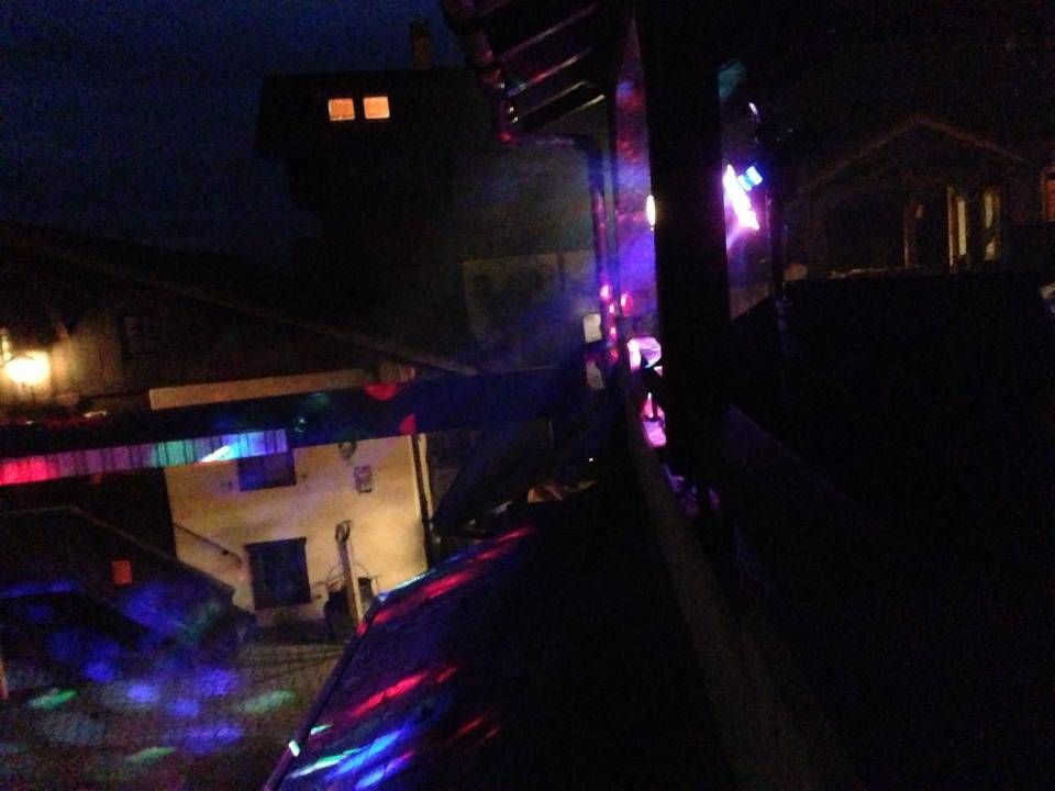 Rue urbaine nocturne avec des néons colorés se reflétant sur les bâtiments et le trottoir.