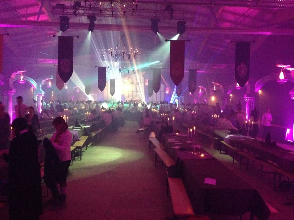 Salle de banquet bondée, éclairée de violet, avec de longues tables et une scène illuminée au loin.