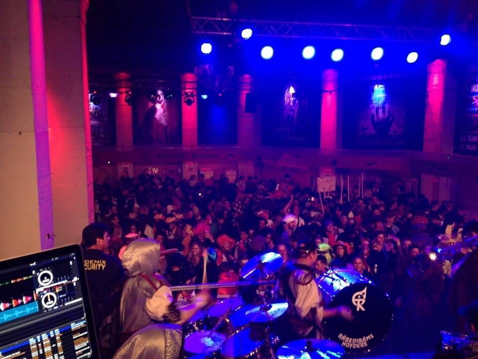 Foule de concert en direct sous des lumières de scène bleues et magenta, avec des musiciens jouant au premier plan