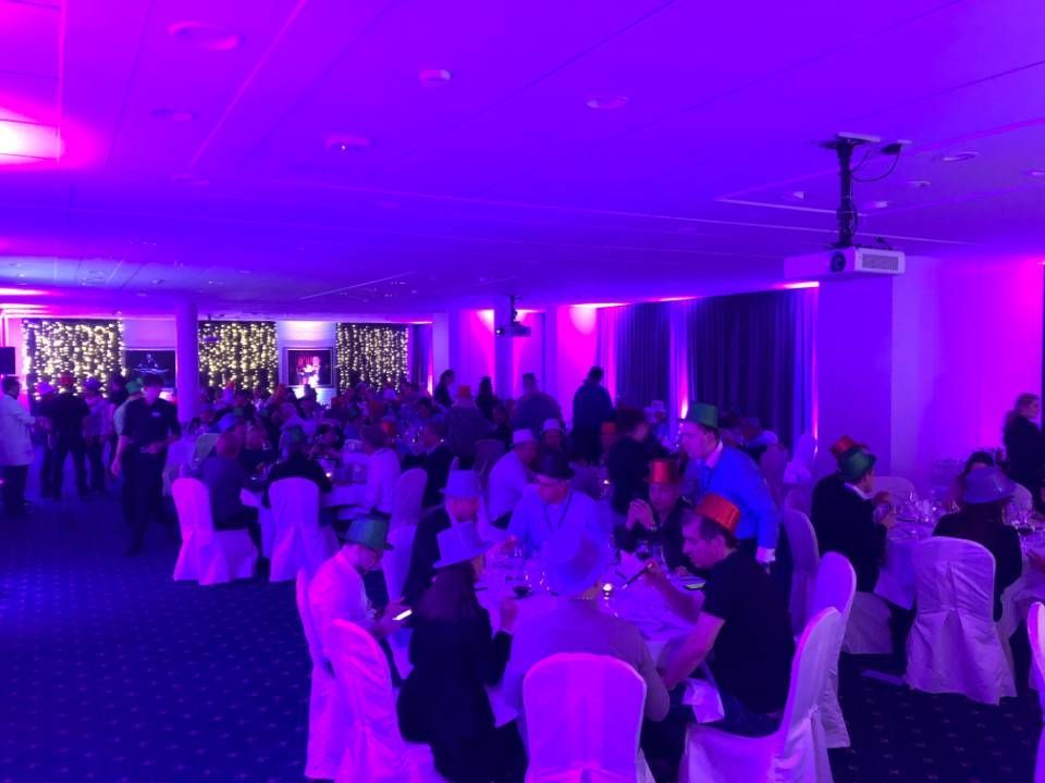 Les invités étaient assis à des tables rondes dans une salle de banquet éclairée de violet, avec des housses de chaises blanches et des appliques murales lumineuses.