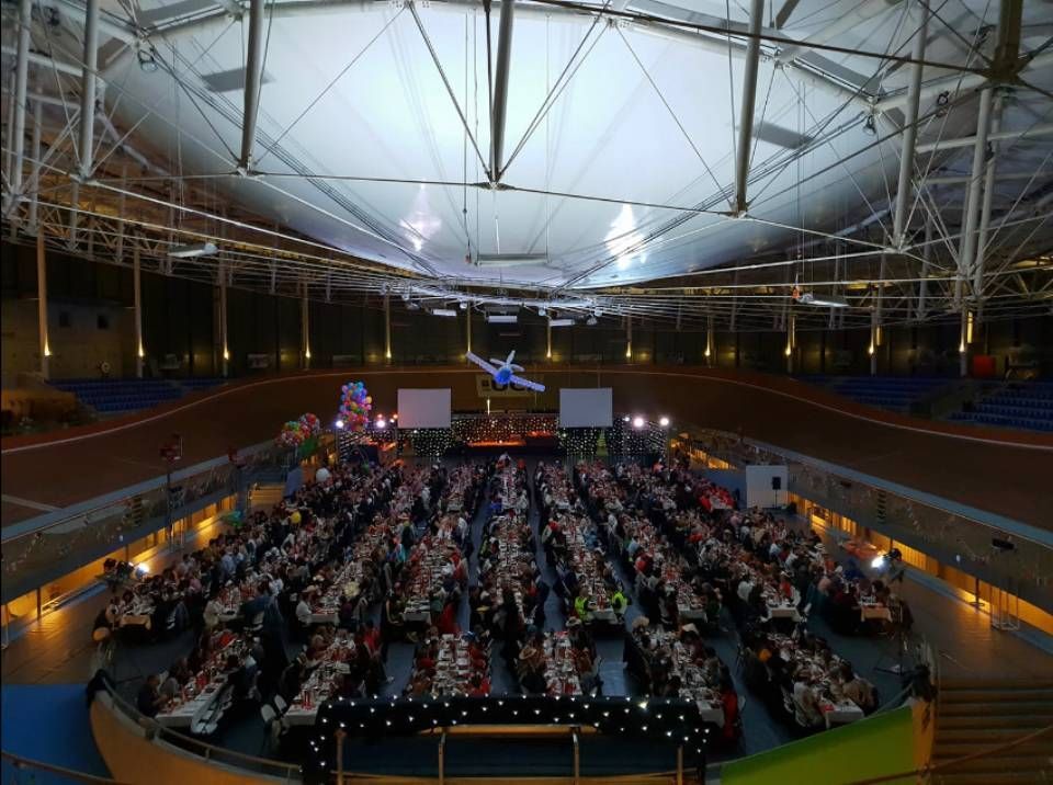 Grand auditorium intérieur rempli de spectateurs assis sous un plafond en dôme lumineux et deux écrans de scène.