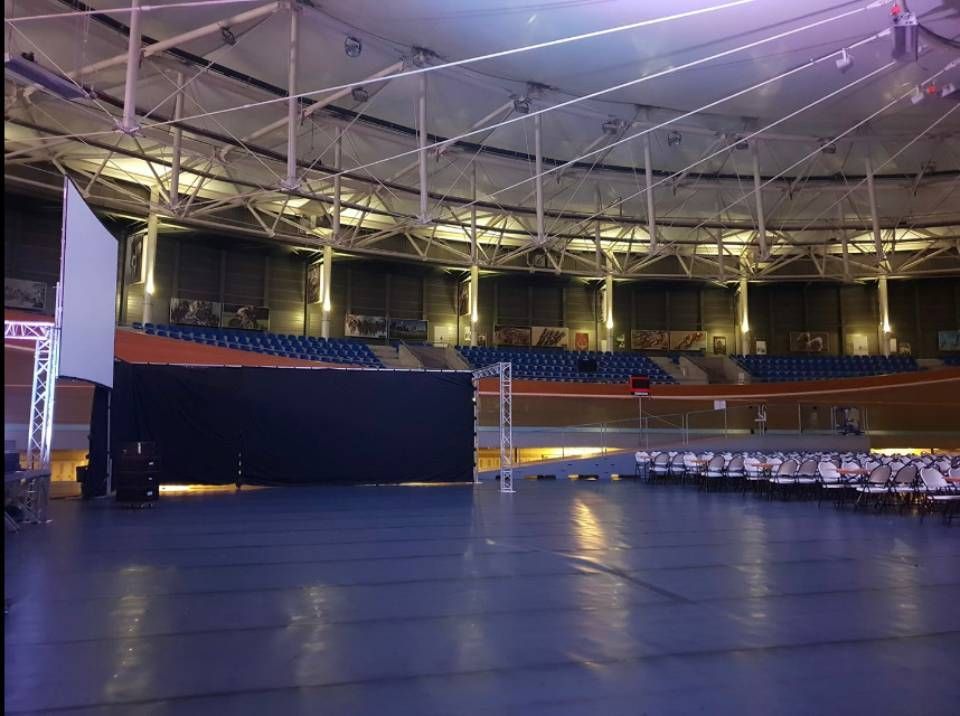 Arène sportive intérieure vide, avec un sol bleu, des rangées de sièges et un éclairage de scène au plafond.