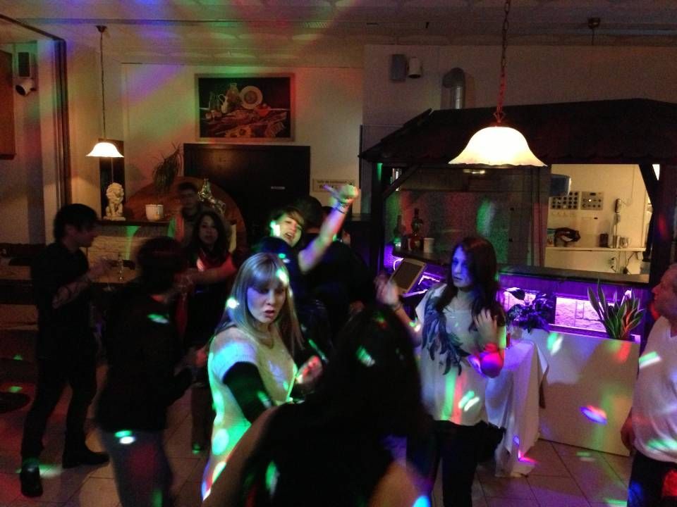 Des gens dansent dans une pièce tamisée, éclairée par des lumières disco colorées et une lampe suspendue.