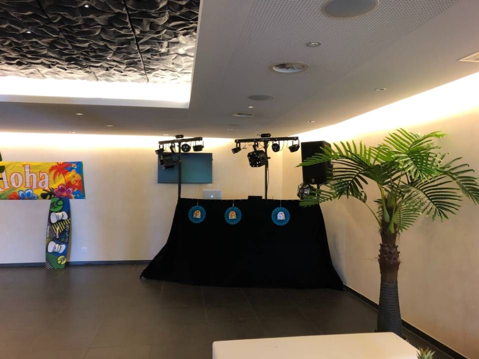 Espace événementiel intérieur avec une scène noire, des éclairages zénithaux et un palmier en pot contre un mur.