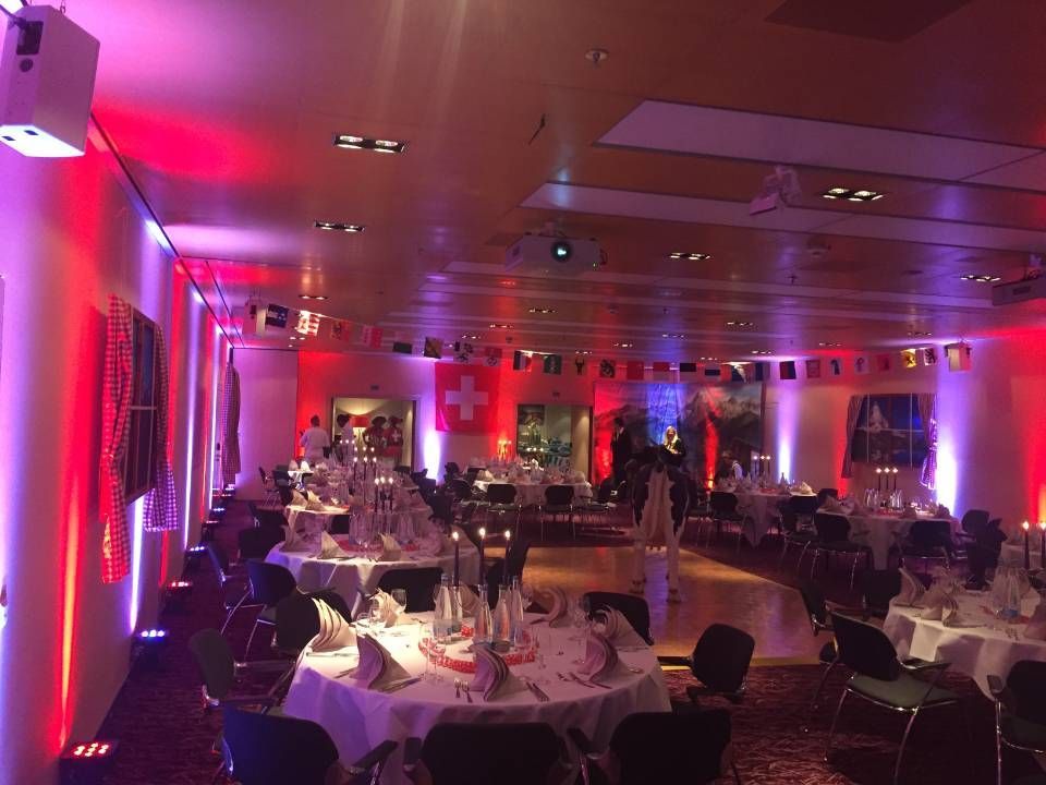 Salle de banquet à l'éclairage tamisé, avec tables rondes, chaises blanches et éclairage d'ambiance rose-violet.