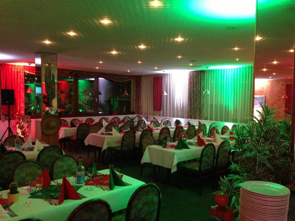 Une salle de banquet faiblement éclairée, avec des nappes blanches, des serviettes rouges et un éclairage d'ambiance vert.
