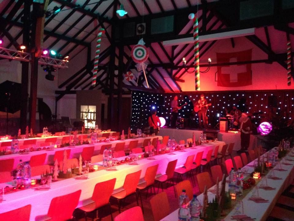 Salle de banquet festive avec de longues tables, un éclairage rose et des décorations suspendues.