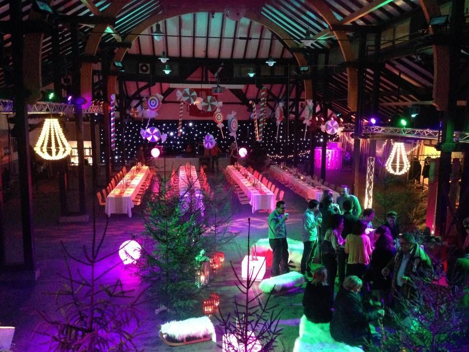 Réception dans une grange décorée avec de longues tables, des lumières violettes et vertes scintillantes, et les invités rassemblés d'un côté